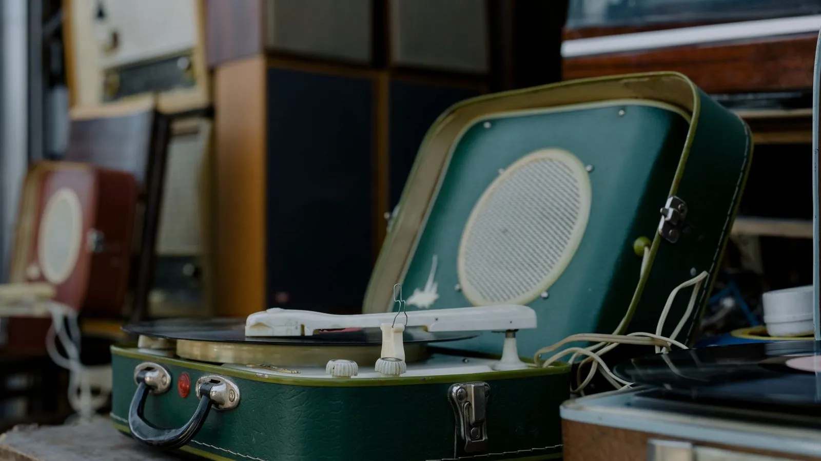 Tocadiscos de maleta antiguo en verde con la tapa abierta junto a otros equipos de audio retro